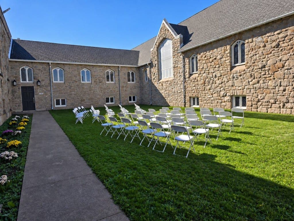 White ceremony chairs on the private lawn beside the stone building