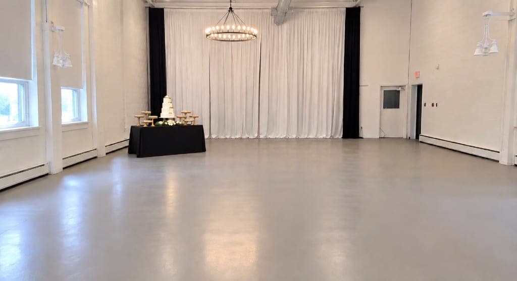 Reception hall with a cake table, white draped backdrop and a ring chandelier
